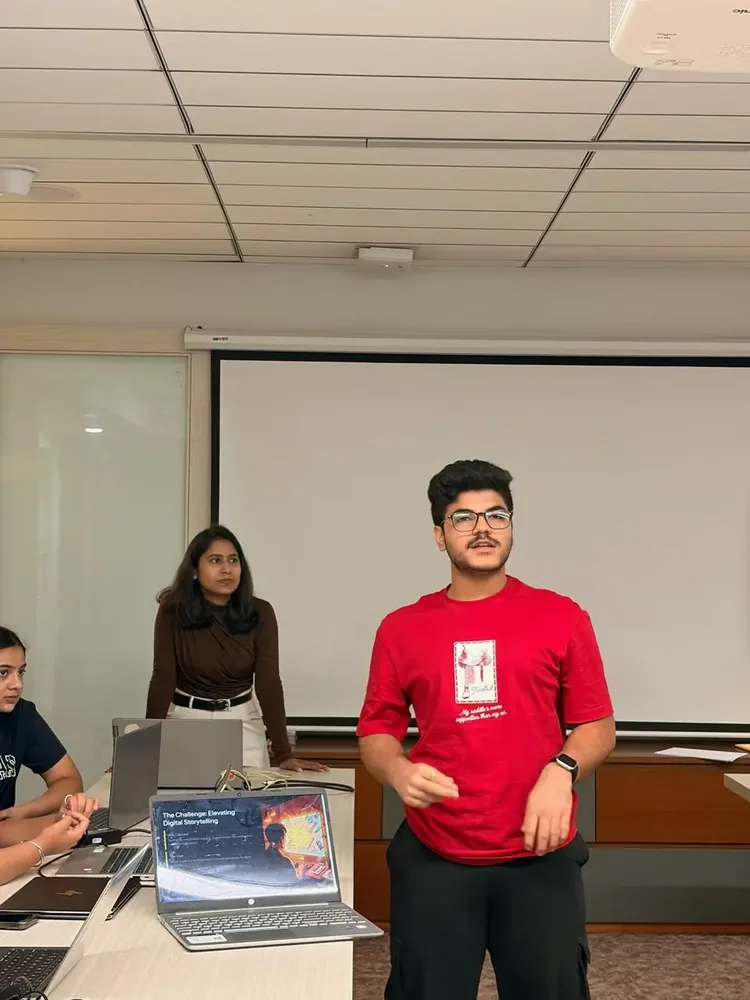 Student standing to present a project while classmates follow on laptops