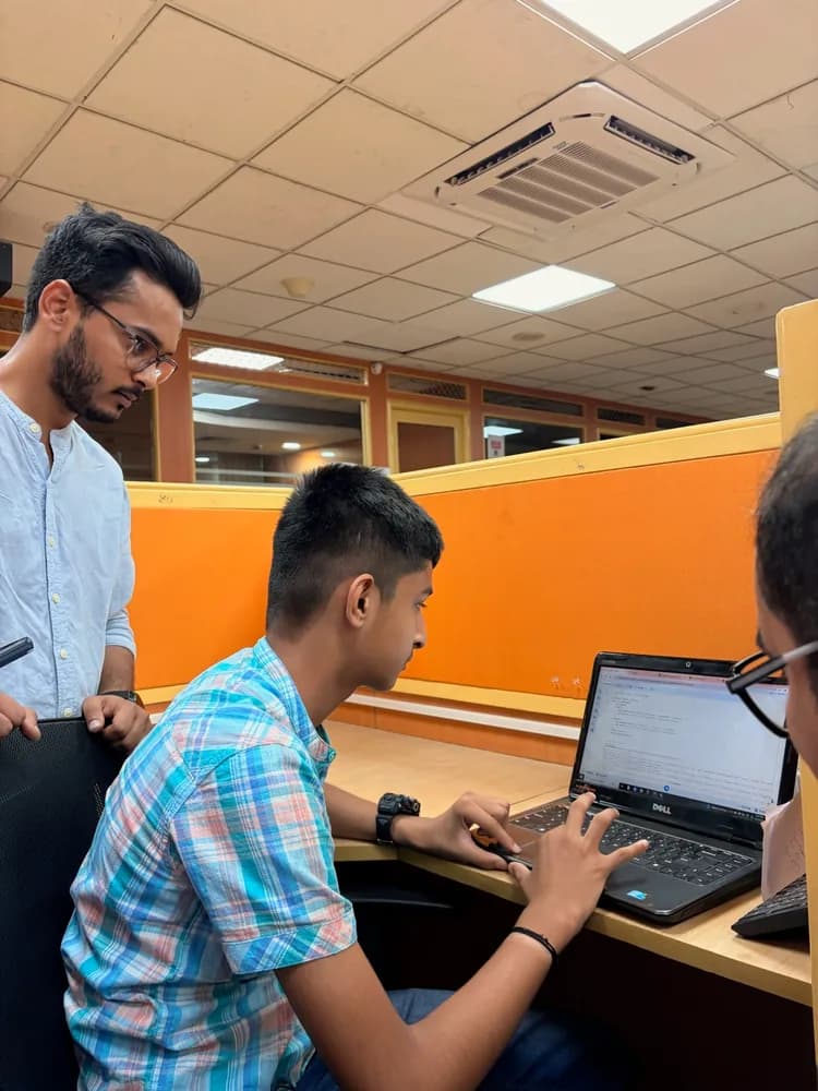 Mentor looking on as a teenager writes code at an office desk