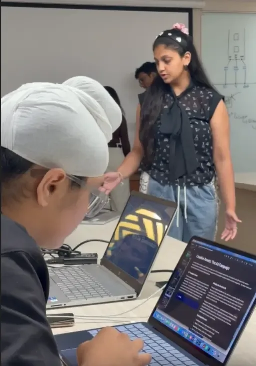 Two students discussing a project brief on laptops beside a whiteboard