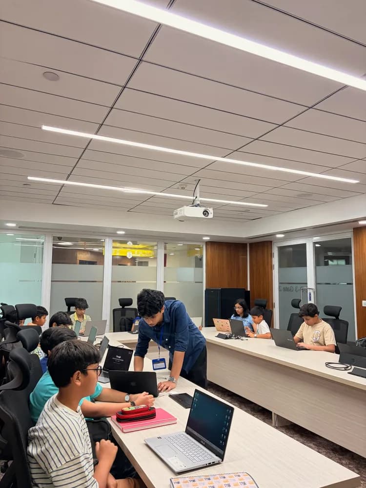 Mentor helping students at laptops around a U-shaped classroom table